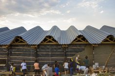 several people are standing in front of a building with metal roofing and fencing around it