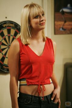 a woman standing in front of a dart board with her hand on her hip and looking at the camera