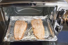 two sandwiches sitting on top of tin foil in an open toaster oven with the door ajar