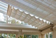 a sun room with lots of windows covered in white blinds and curtains hanging from the ceiling