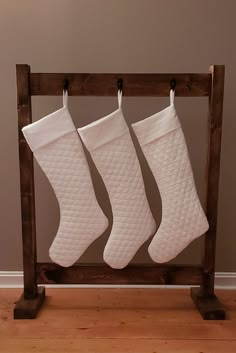 three white christmas stockings hanging from a wooden rack