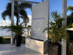 an outdoor fountain surrounded by potted plants and water features in front of a body of water