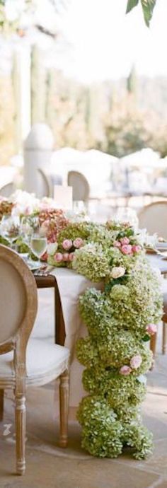 the table is set with white and pink flowers on it, along with two chairs