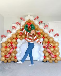 a woman standing in front of a gingerbread arch with balloons and candy canes