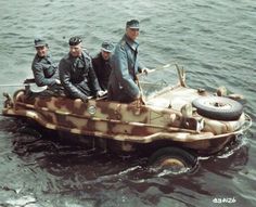 three men are riding in an old fashioned speedboat on the water while another man stands next to them