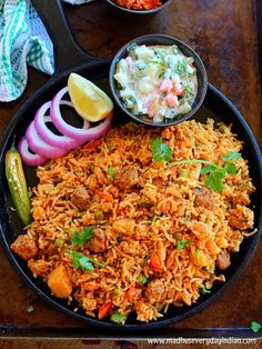 mexican rice with meat and vegetables in a black bowl on a wooden table next to a side dish