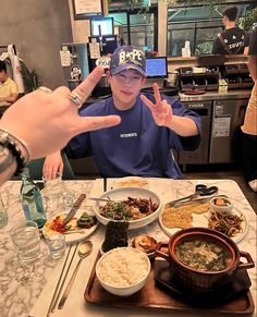 a person sitting at a table with food in front of him and two hands up