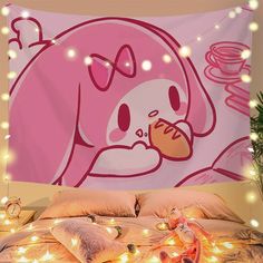 a pink hello kitty wall hanging over a bed covered in blankets and pillows with fairy lights