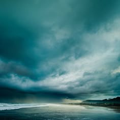 the sky is very dark and cloudy over the ocean on a stormy day at the beach