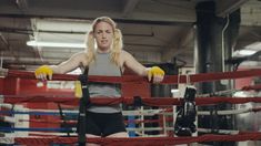 a woman standing in front of a boxing ring with gloves on her hands and yellow gloves hanging from the ropes