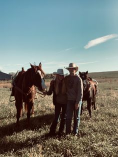 two people standing next to horses in a field