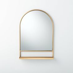 a mirror mounted to the side of a white wall next to a shelf with a gold frame