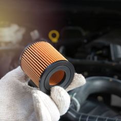 a close up of a person holding a air filter in front of a car engine