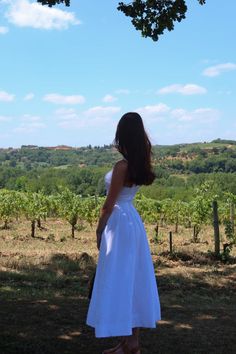 a woman in a white dress looking at the vineyard