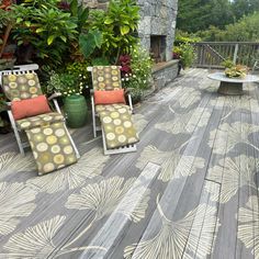 two lawn chairs sitting on top of a wooden deck next to potted plants and trees