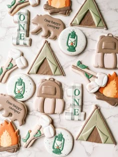 decorated cookies with camping related items displayed on a marble countertop, including campfire and backpack