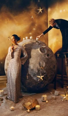 two people standing in front of a large rock with stars on it and candles around it