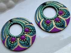 two colorful earrings are sitting on a white surface, one is purple and the other is green