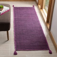 a purple rug with tassels on the floor next to a chair and window