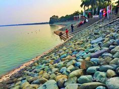 people are standing on the shore of a lake with rocks and stones in front of them