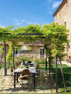 an outdoor dining area with table and chairs under a pergolated trellis on the lawn