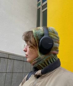 a woman wearing headphones and a knitted hat in front of a yellow building