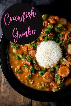 a black bowl filled with gumbo and rice on top of a wooden table next to a spoon