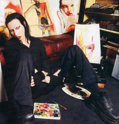 a woman sitting on top of a couch in front of paintings and paintbrushes