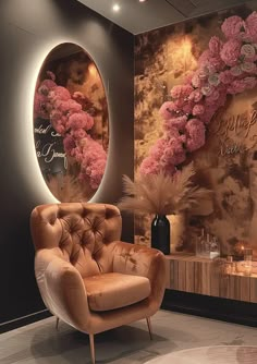 a chair in front of a wall with flowers on it and a round mirror behind it