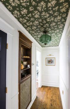 the hallway is decorated with green and white wallpaper, wood flooring, and an ornate ceiling