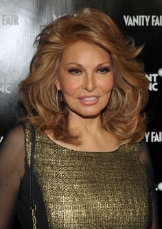 an older woman with blonde hair and gold dress posing for the camera in front of a black background