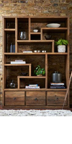 a wooden bookcase with many drawers and plants on the top, in front of a brick wall