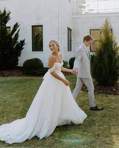 a bride and groom holding hands in front of a white brick house on their wedding day