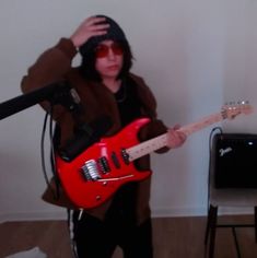 a person holding a red guitar in front of a microphone and recording equipment on a tripod