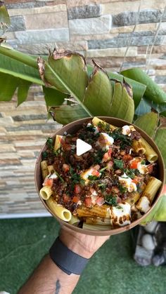 a person holding a bowl filled with pasta and sauce on top of a green surface