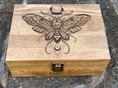 a wooden box with an intricately carved moth on the front and side, sitting on top of a rock