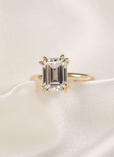 an emerald - cut diamond sits on top of a white satin material with gold accents