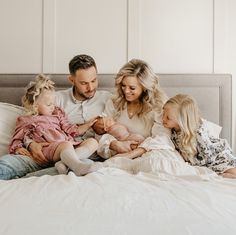 a man and two women sit on a bed with their three children, who are all looking at each other