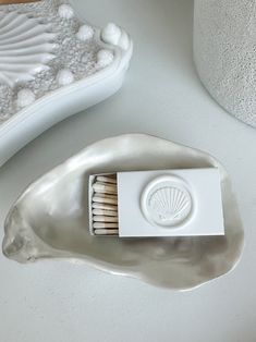 a matchbox sitting on top of a silver shell shaped ashtray next to a white vase