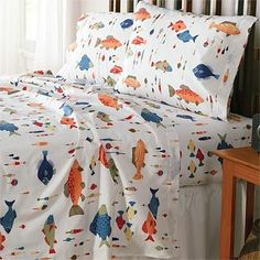 a bed with white sheets and colorful fish on it's cover, next to a night stand