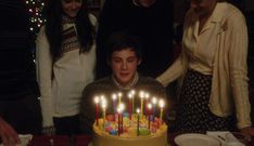 a young man sitting in front of a birthday cake with lit candles on top of it