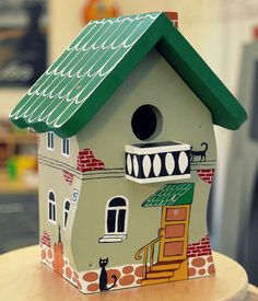 a birdhouse with a cat sitting on top of it's roof and windows