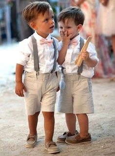 two young boys standing next to each other on a dirt road with people in the background