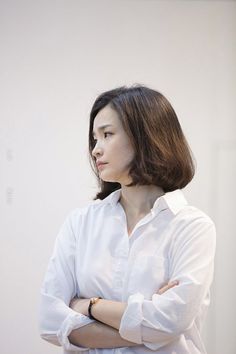 a woman standing with her arms crossed and looking off to the side, wearing a white shirt