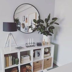 a white shelf with baskets, books and a mirror on the wall in a living room