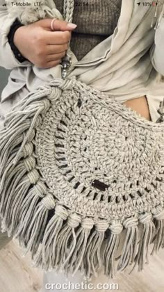 a woman is holding a crocheted bag with fringes on the bottom and sides