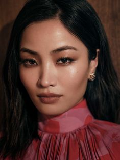 a woman with dark hair wearing a red shirt and earrings, posing for the camera