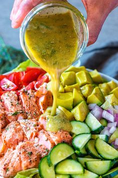 someone pouring dressing over a salad with salmon and cucumbers