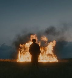 a man standing in front of a large fire with lots of flames coming out of it