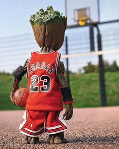 a baby groote is holding a basketball in his hands and wearing an orange jersey